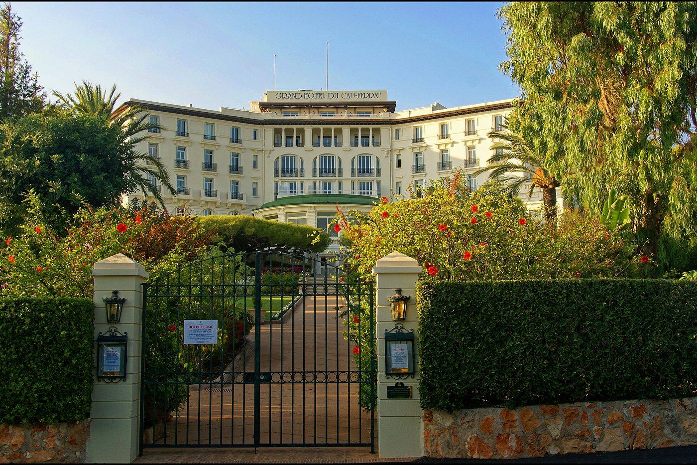 The gate and garden approach to Grand-H&ocirc;tel du Cap-Ferrat, with hibiscus along the drive