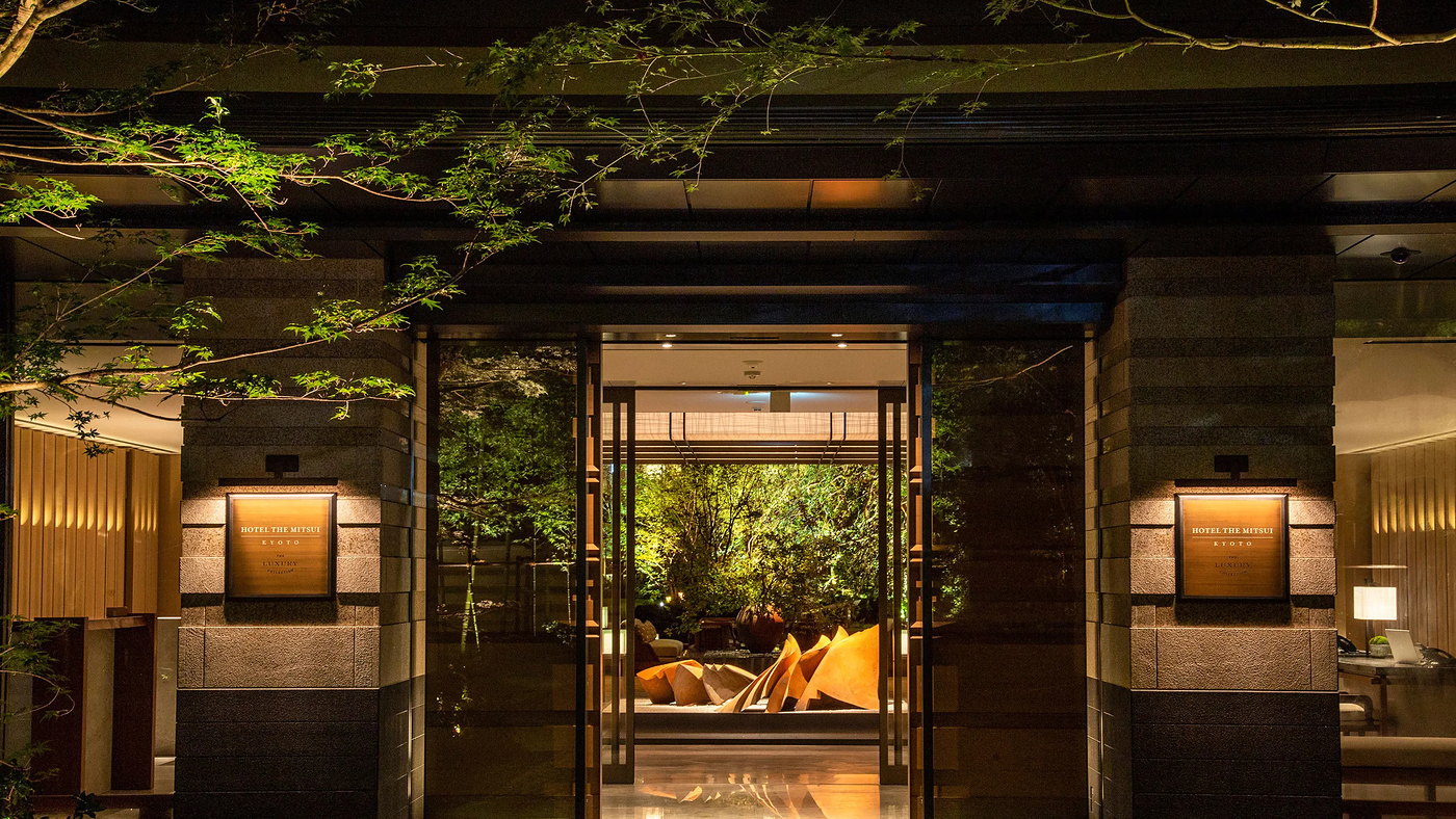 The Kajiimiya Gate lit at night at HOTEL THE MITSUI KYOTO, maples overhead and the lobby beyond