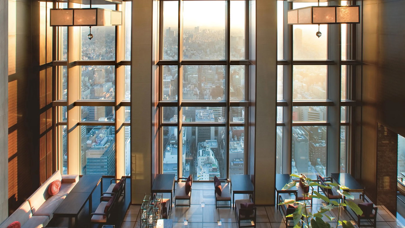 A double-height lounge at Mandarin Oriental Tokyo at sunset, tall windows over the city