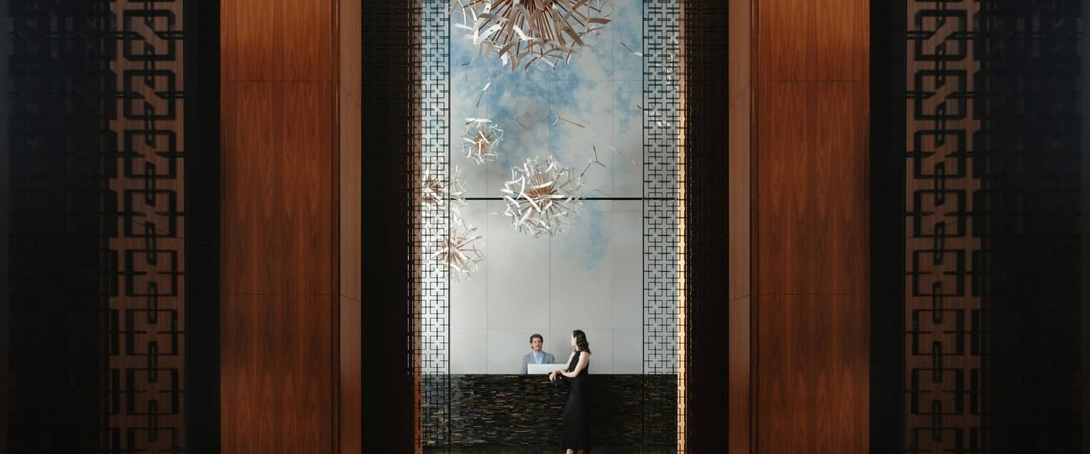 Two guests seated in a hotel lobby beneath a sculptural artwork