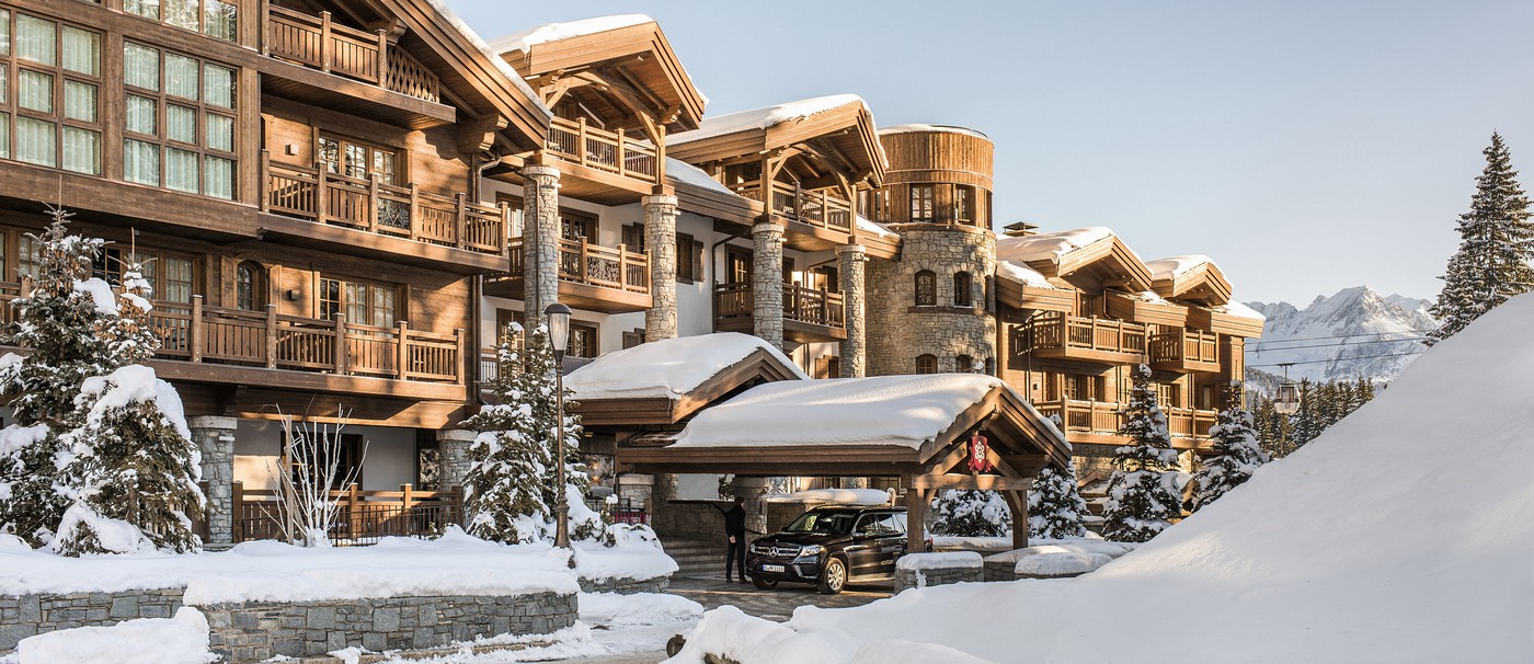 L'Apogee Courchevel in the Jardin Alpin at first light, a car waiting under the porte-cochere
