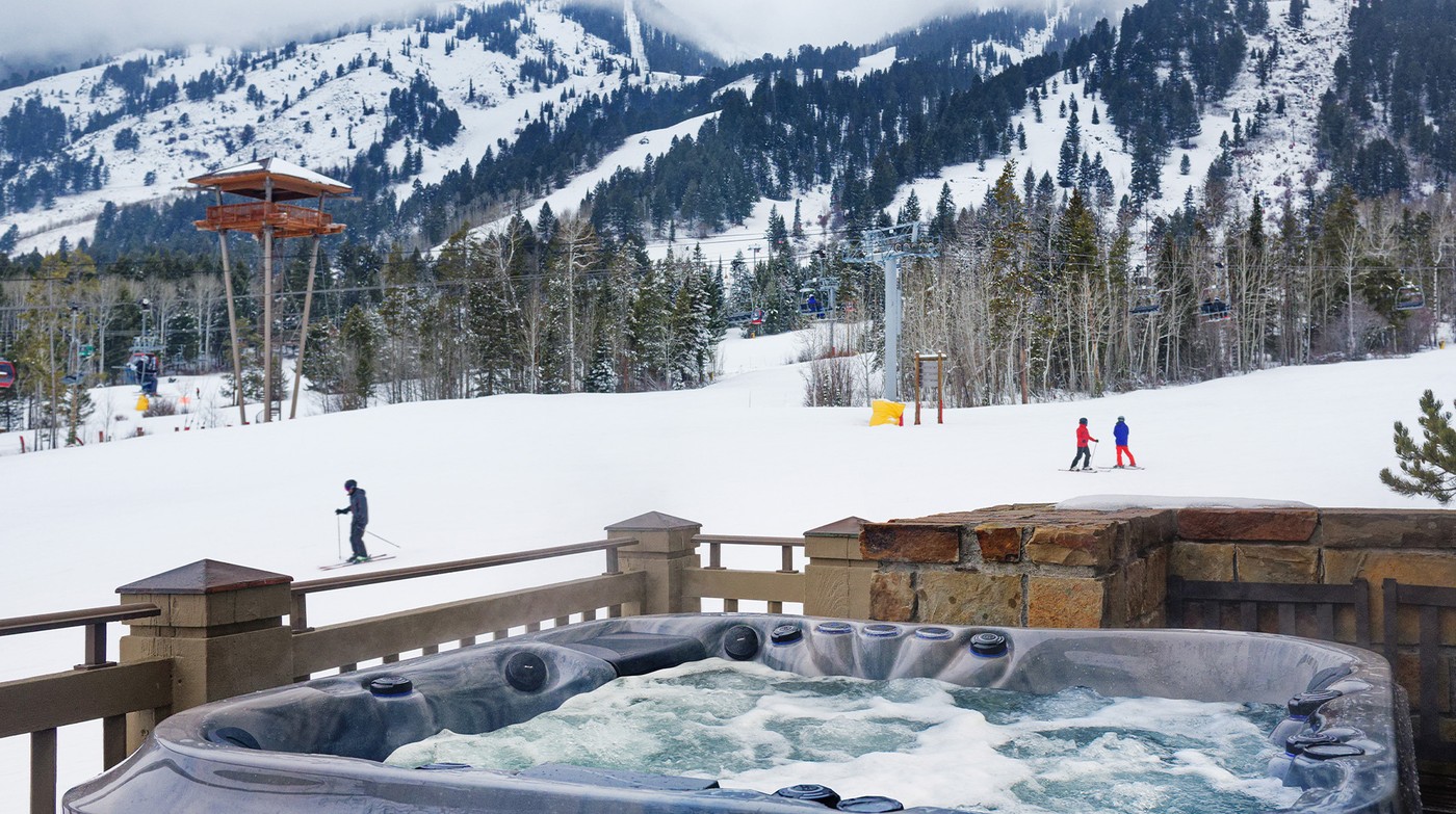 An outdoor hot tub at Teton Village, skiers crossing the run and the lifts turning behind