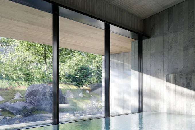A stone-lined indoor onsen bath with full-height glazing onto a mossy rock garden and forest
