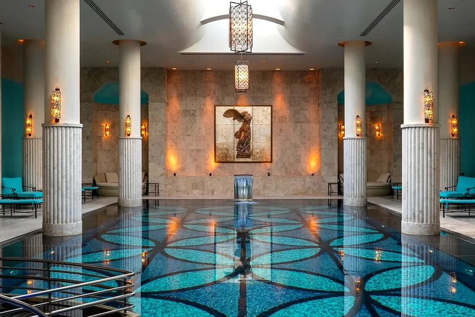 A colonnaded indoor swimming pool lit by lanterns, loungers along both sides