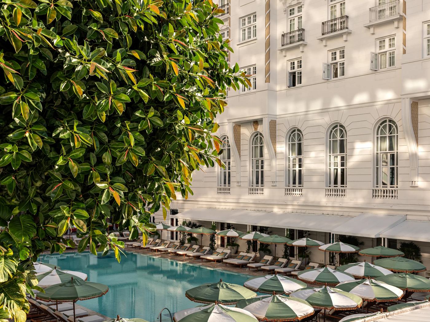 The pool and white facade of Copacabana Palace, Rio de Janeiro, with green and white fringed parasols