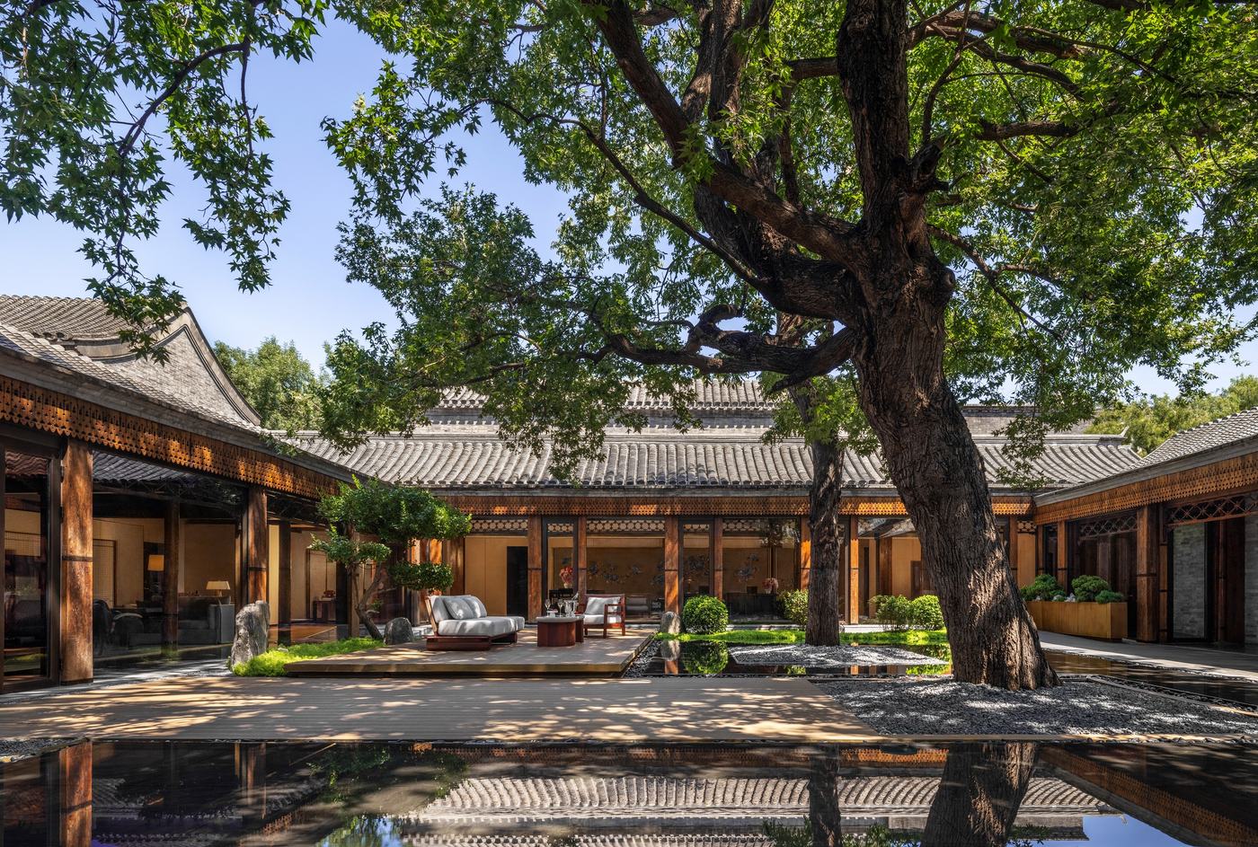 A courtyard at Mandarin Oriental Qianmen, Beijing, with grey tiled roofs, a mature tree and a reflecting pool