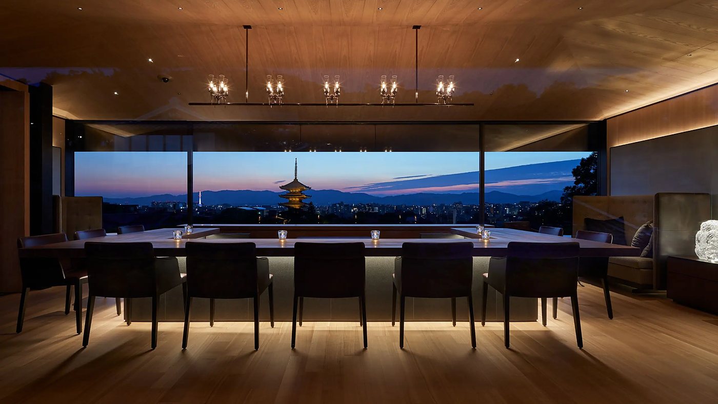 A private dining room at Park Hyatt Kyoto at dusk, the Yasaka Pagoda and the lit city framed through a full-width window