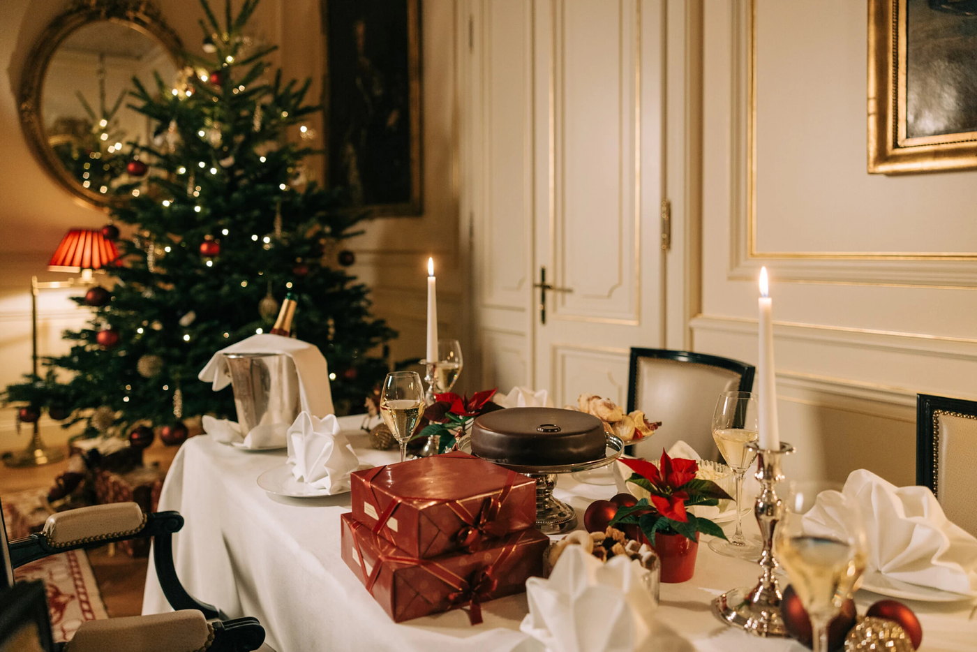 A table laid for Christmas dinner at Hotel Sacher Wien, candles and wrapped gifts, a lit tree behind